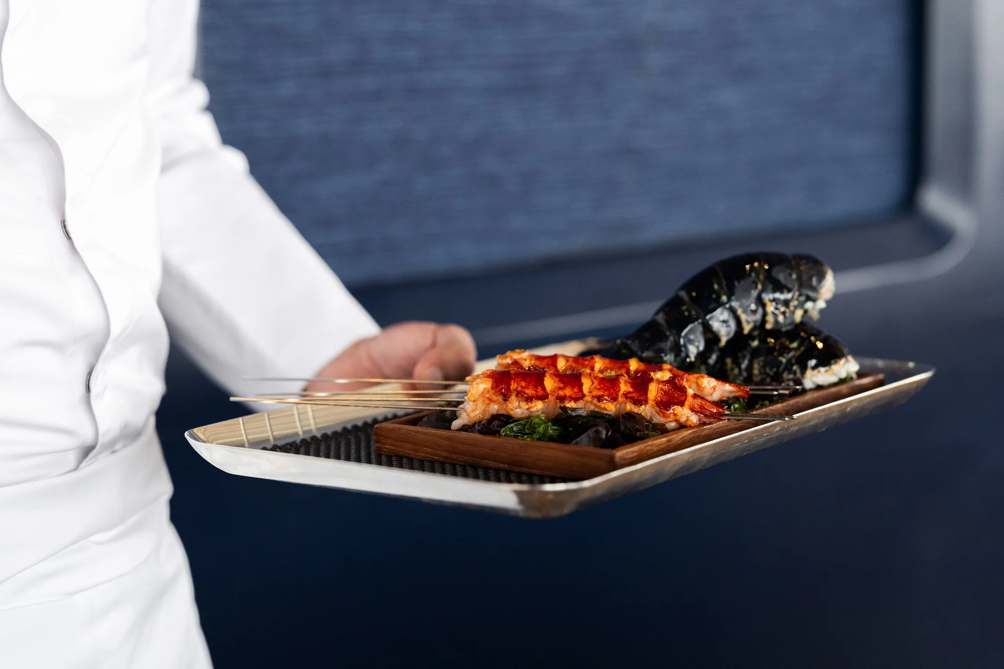 A member of the team carrying a tray of lobster skewers during BLUE × AKKEE service.