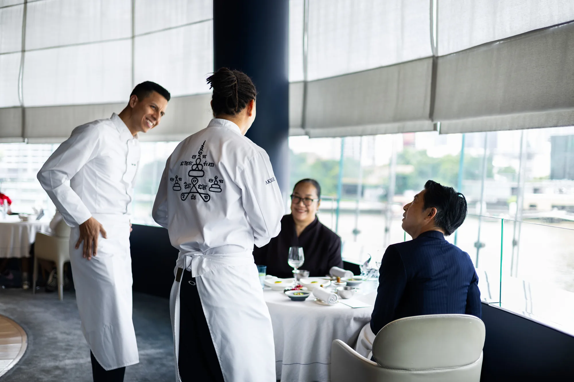 The BLUE and AKKEE chefs greeting diners beside BLUE’s riverfront windows.