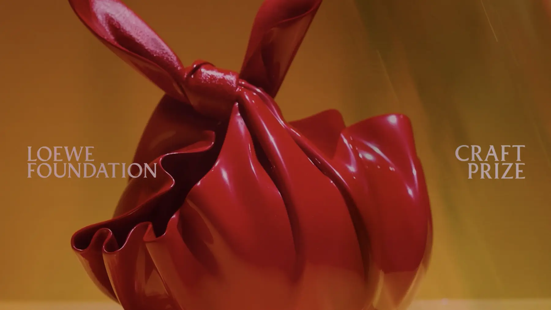 Frame from the opening title of the LOEWE FOUNDATION Craft Prize films: a red sculptural object against amber