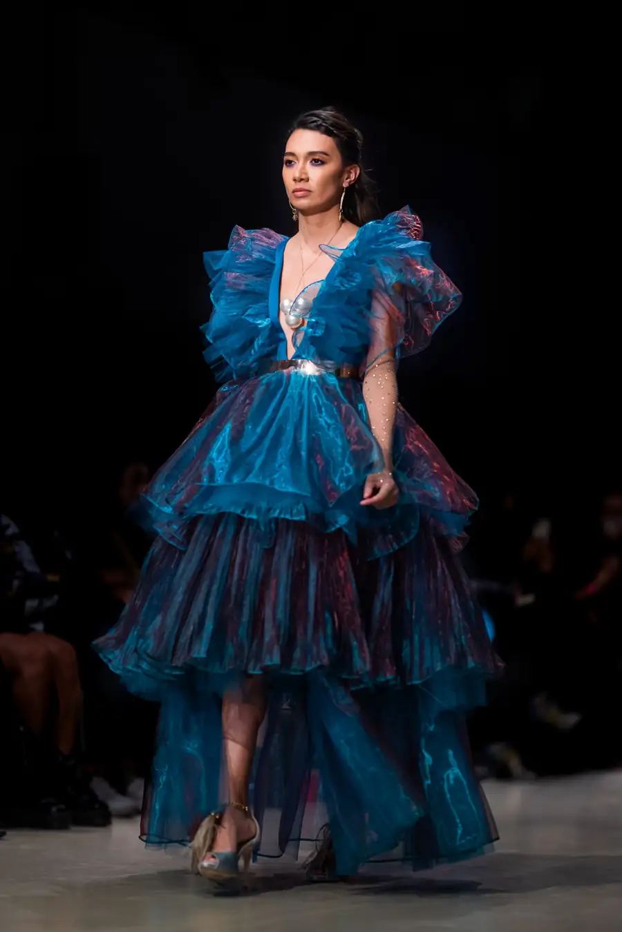 A model on the Vancouver Fashion Week runway in a layered teal organza gown with ruffled shoulders