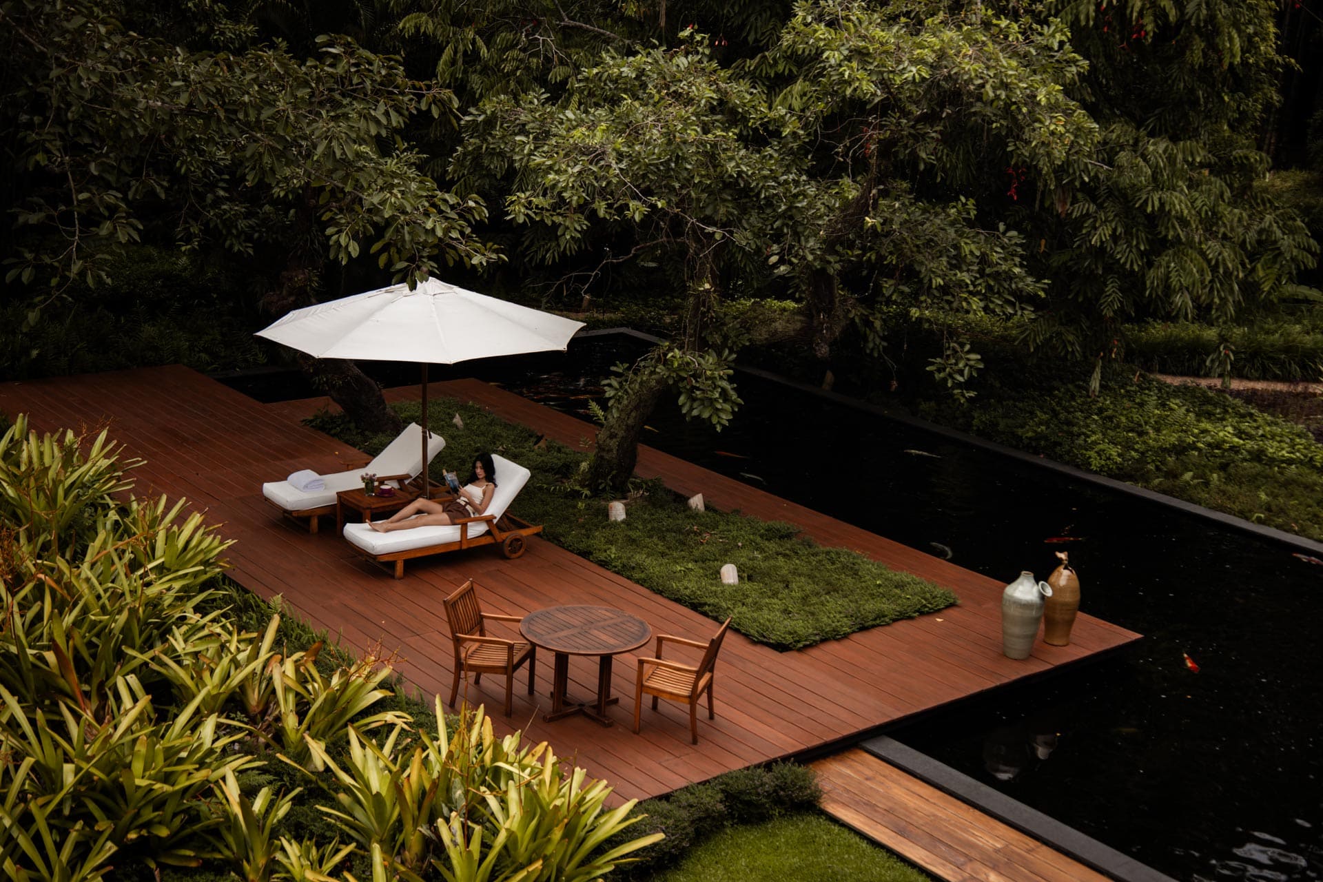 A guest relaxing on Tatvani’s timber pool terrace beneath a white umbrella.