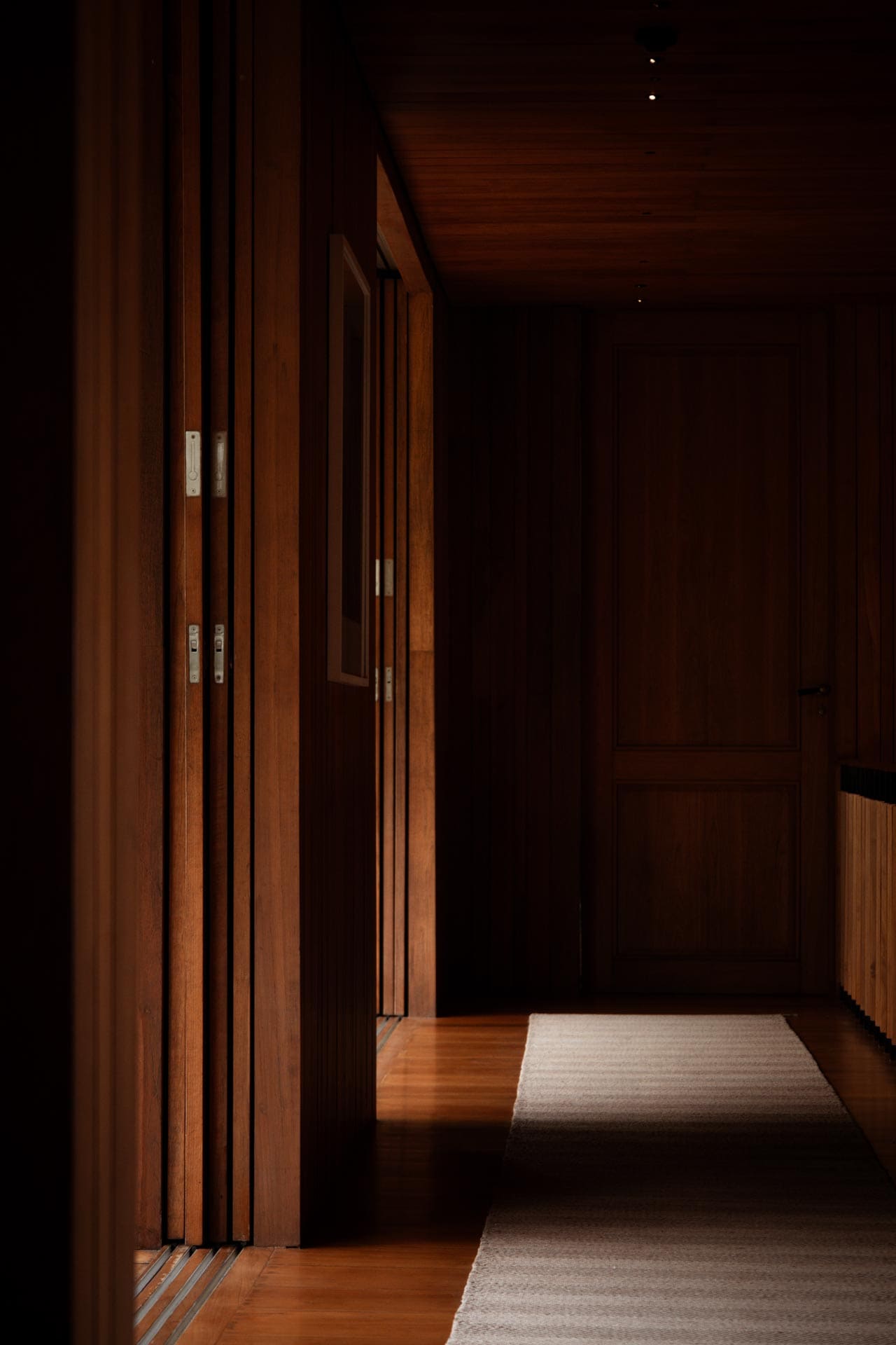 Warm light falls along the timber doors and corridor at Tatvani.