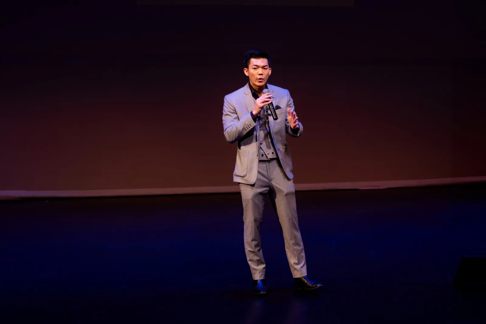 Deejai Riangkrul holding a microphone while speaking on stage.