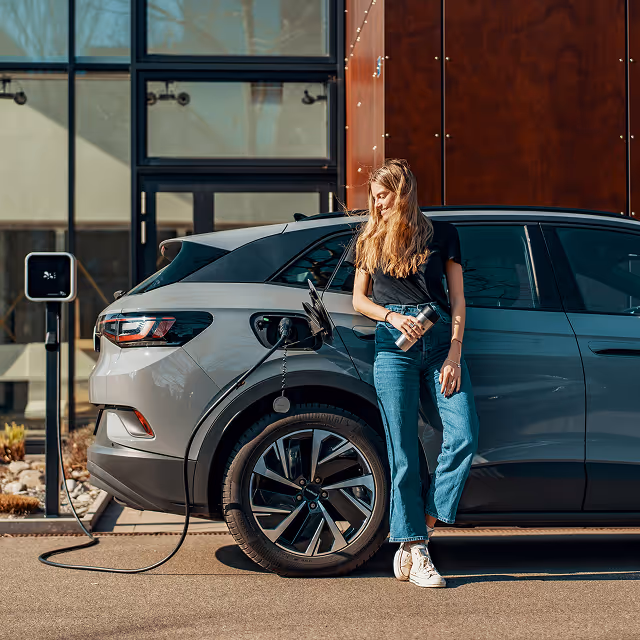 person leaning on their car while it charges