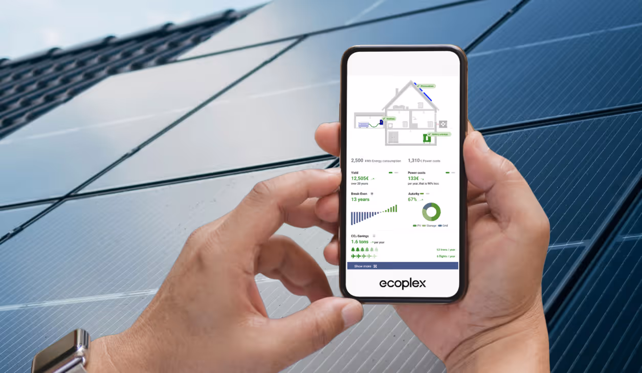 Person holding a smartphone displaying an energy consumption and savings dashboard with solar panel graphics, with solar panels in the background.