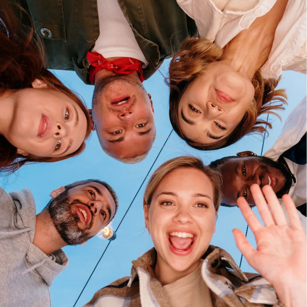 a group six men and women in their 20s to 30s. they are in a circle looking down at the camera. the photo is a closeup of all of their faces.