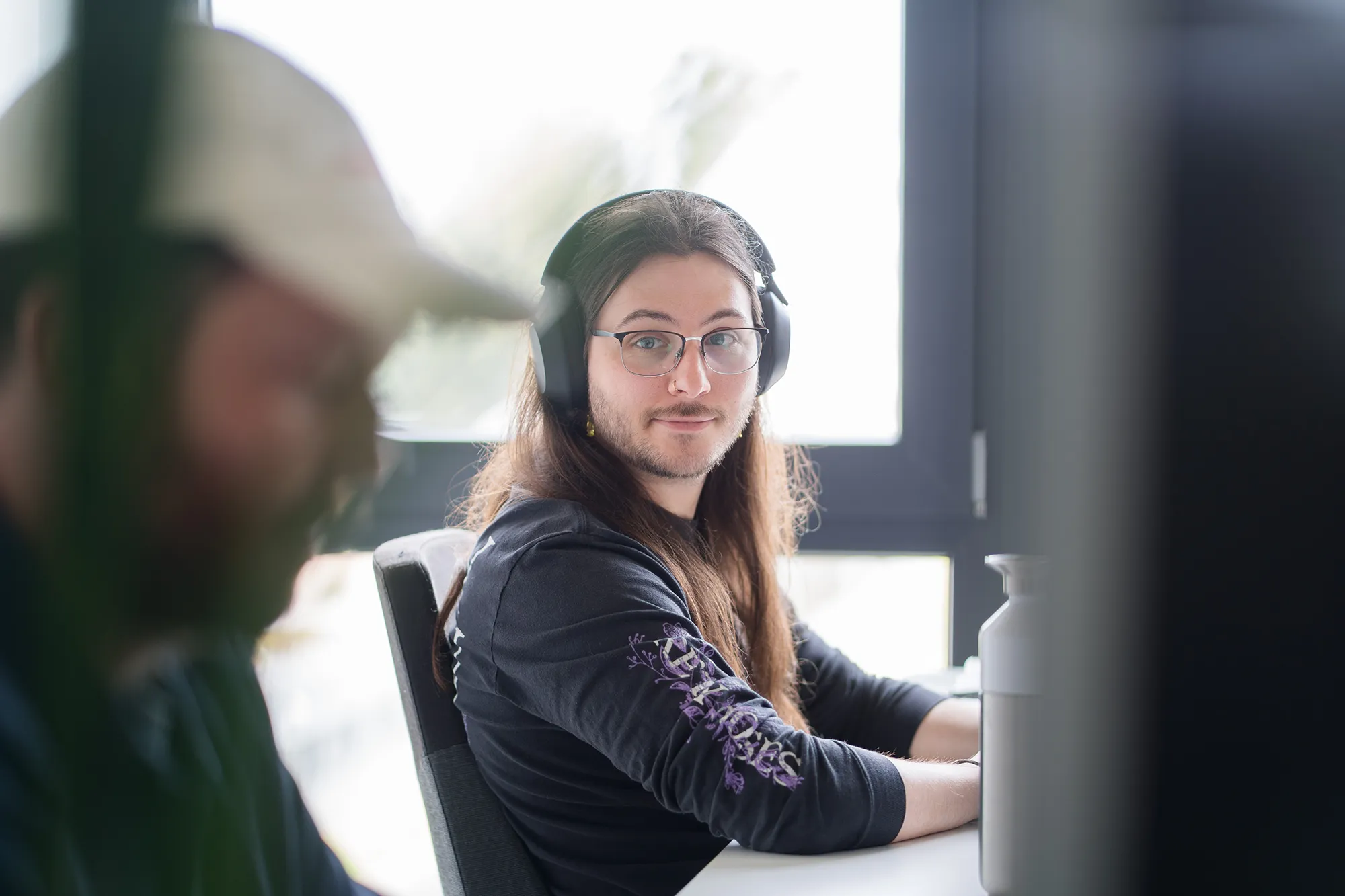 Mitarbeitender sitzt am Schreibtisch und schaut zu seinem Kollegen.