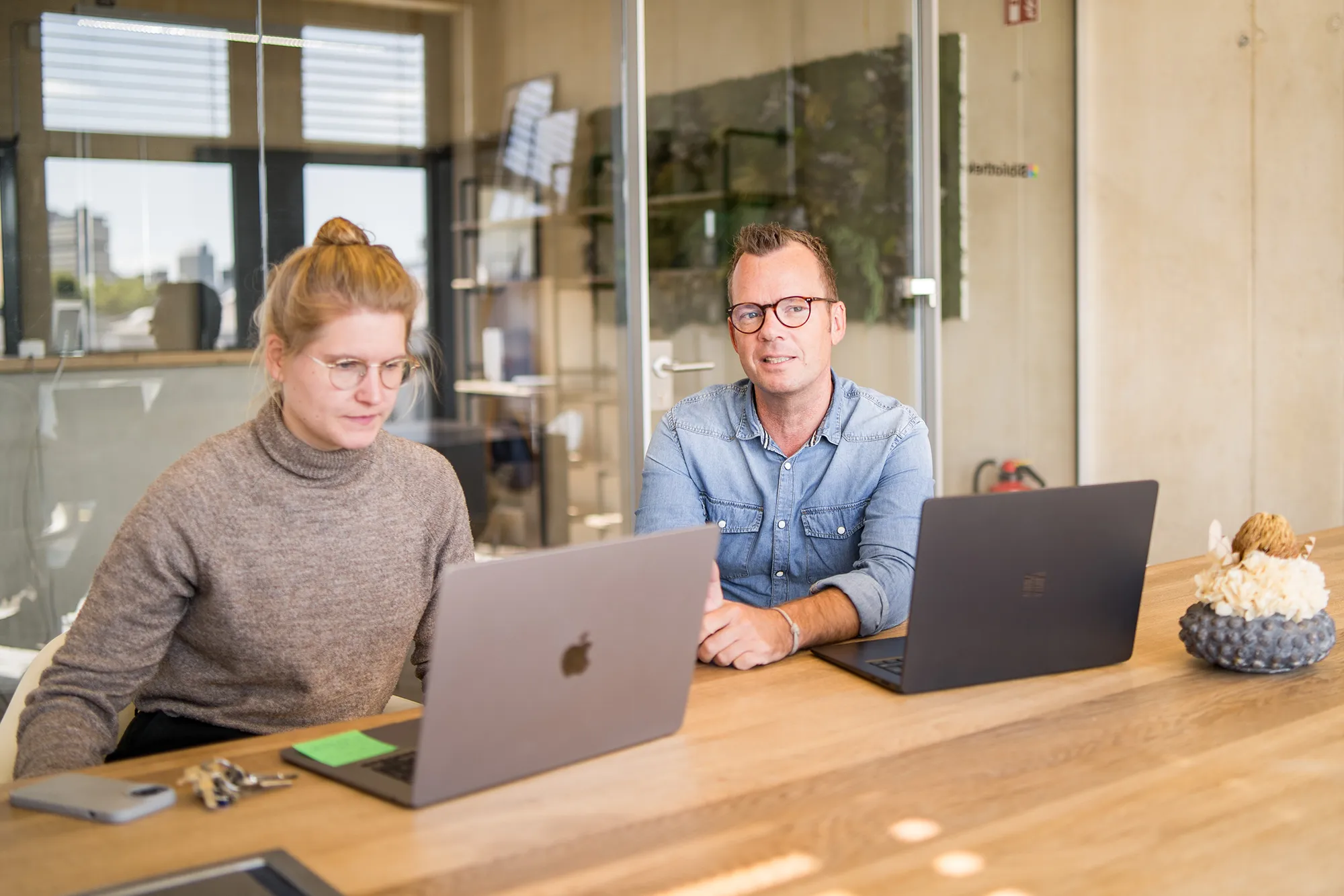 Zwei Mitarbeitende sitzen mit ihren Laptops im Meetingraum.