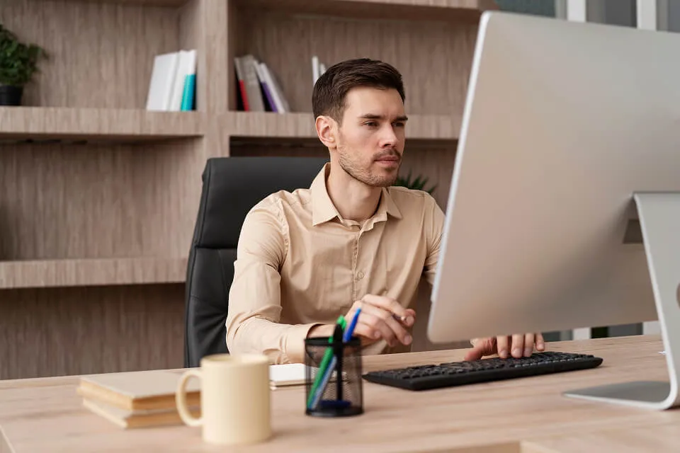 A focused male professional working at a desktop monitor in a modern office.