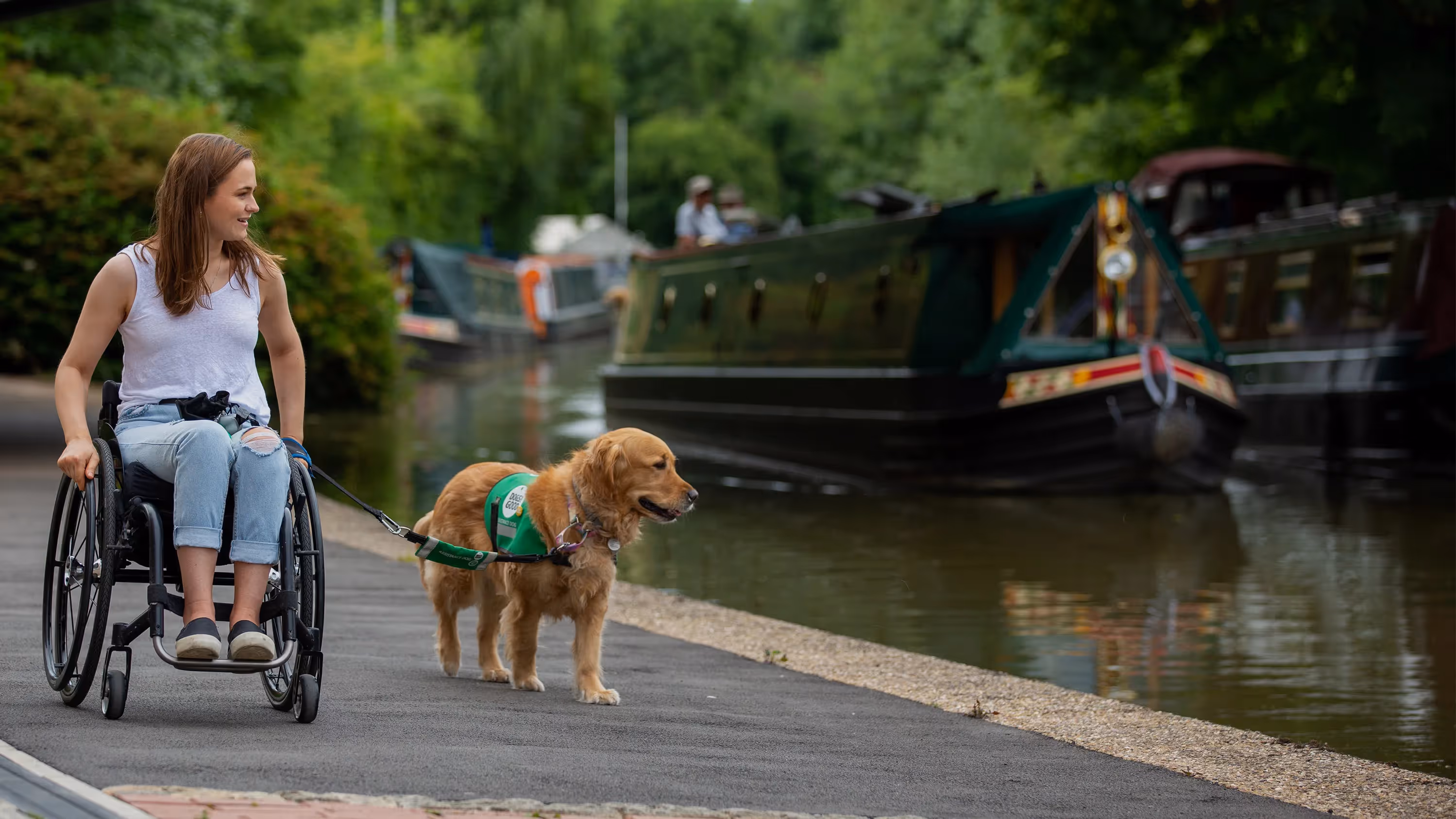 A woman in wheelchair taking her guide dog for a walk along a river.