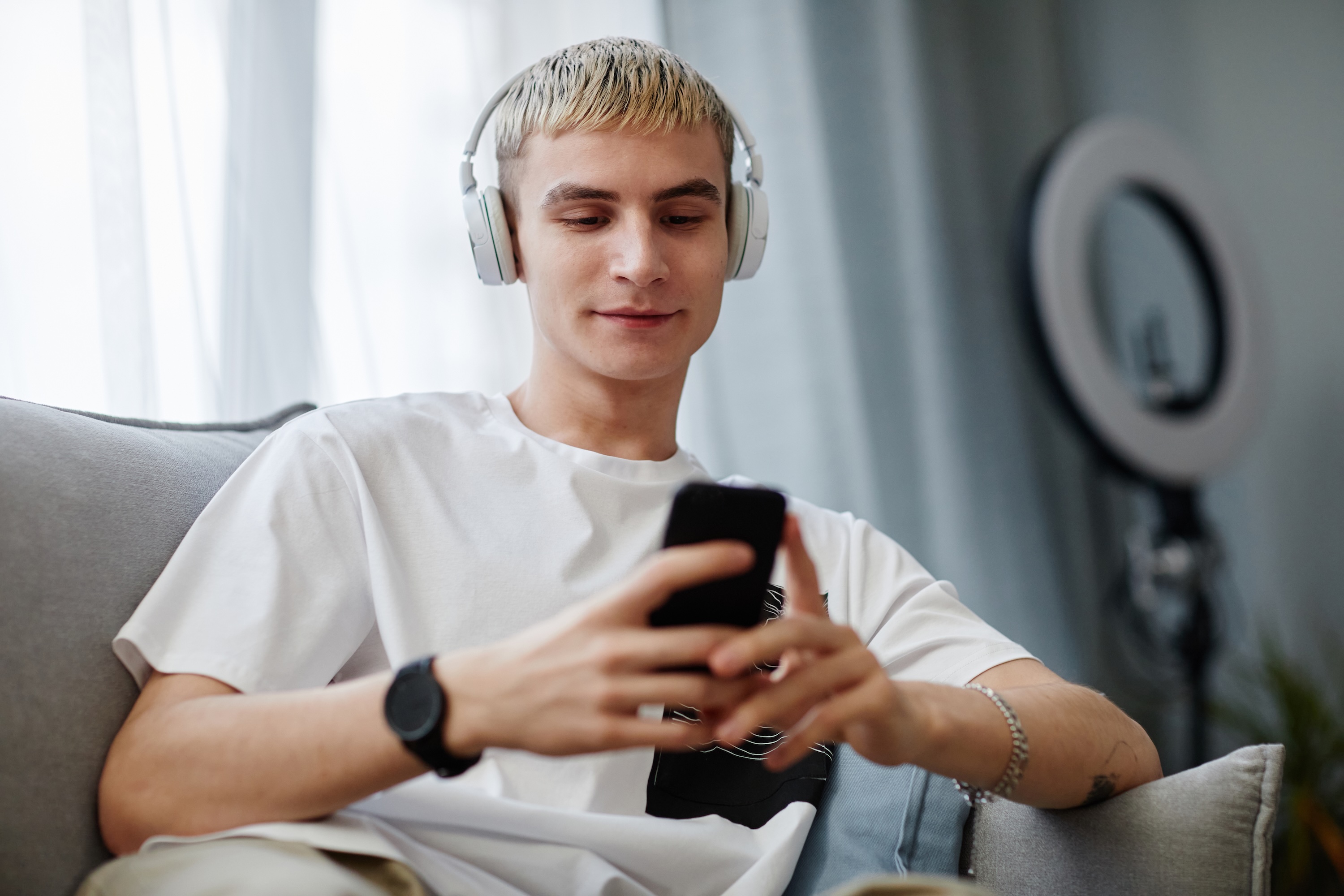 Young person with headphones on holds phone and smiles