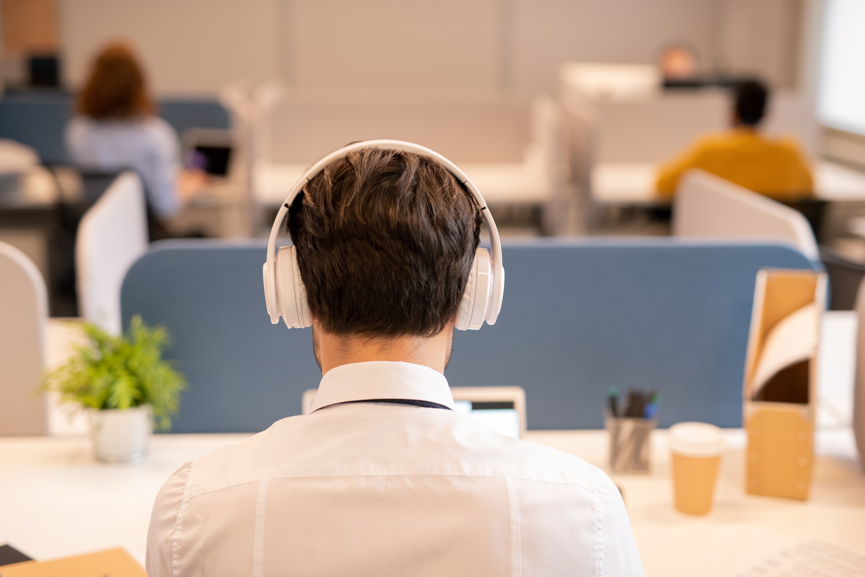 Person sitting with back to the camera at a desk, wearing headphones, working in an office
