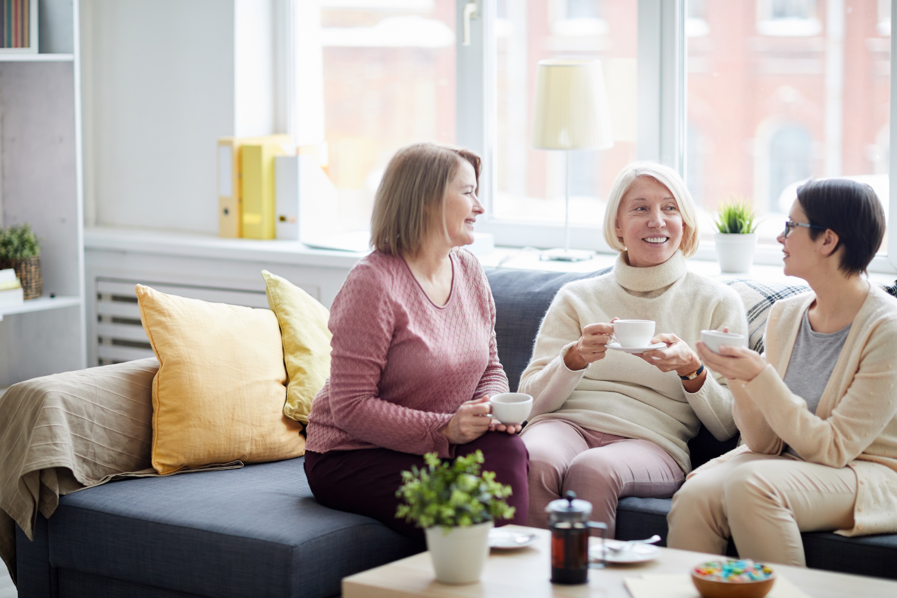 Three women chatting on a sofa with tea