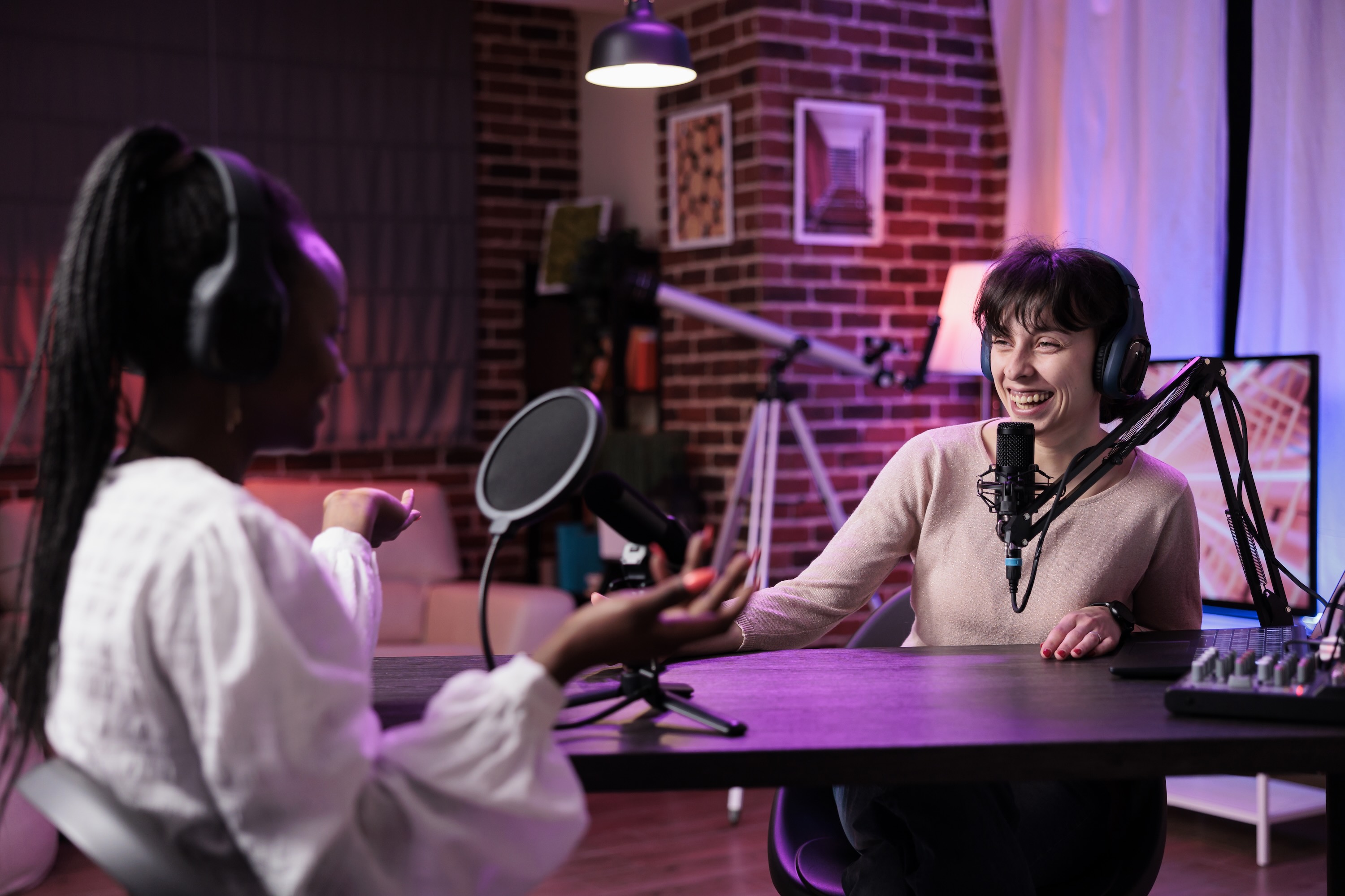 Two people sitting opposite each other recording a podcast and laughing