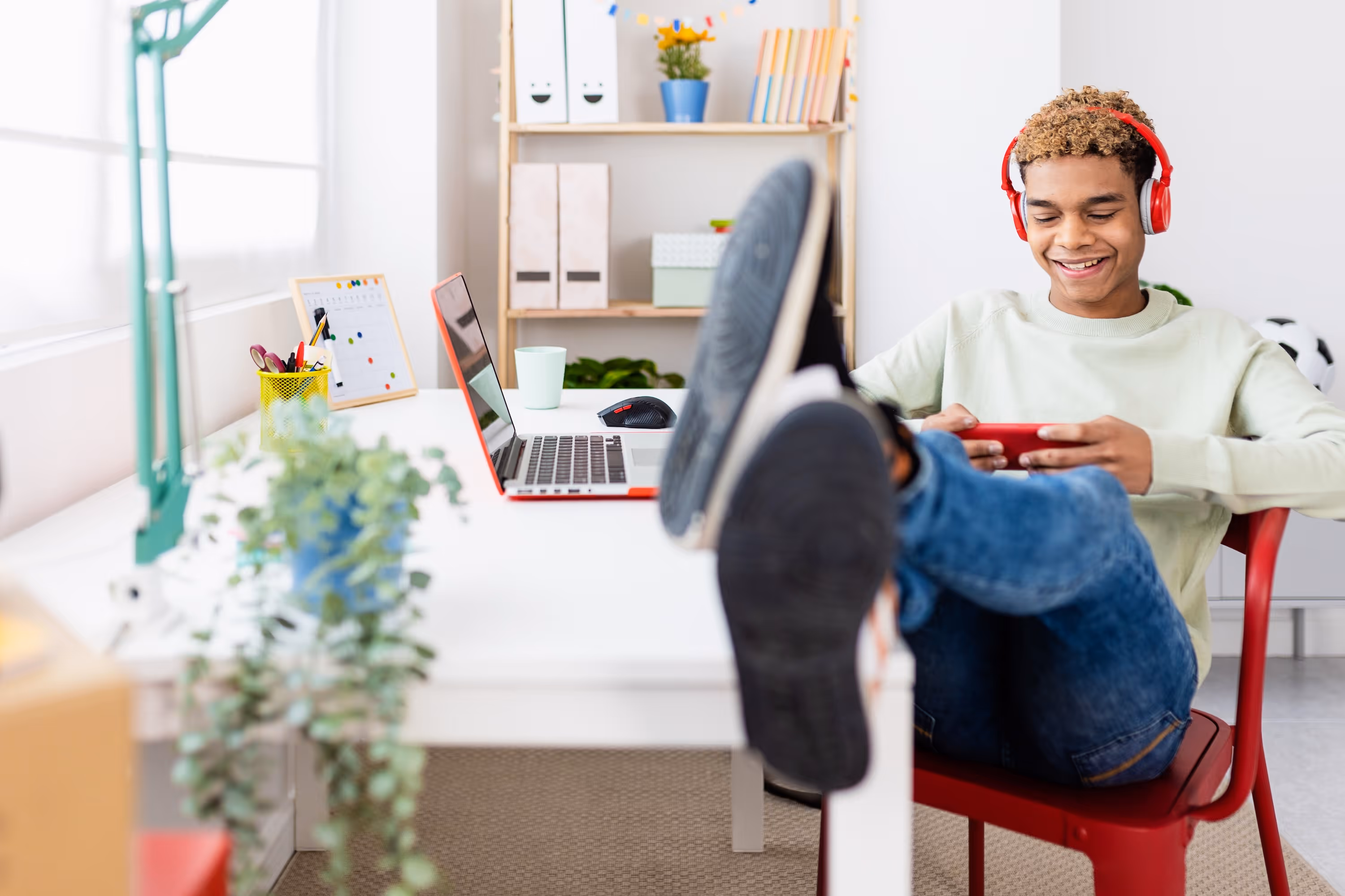 Young man sits in chair with headphones on watching his phone