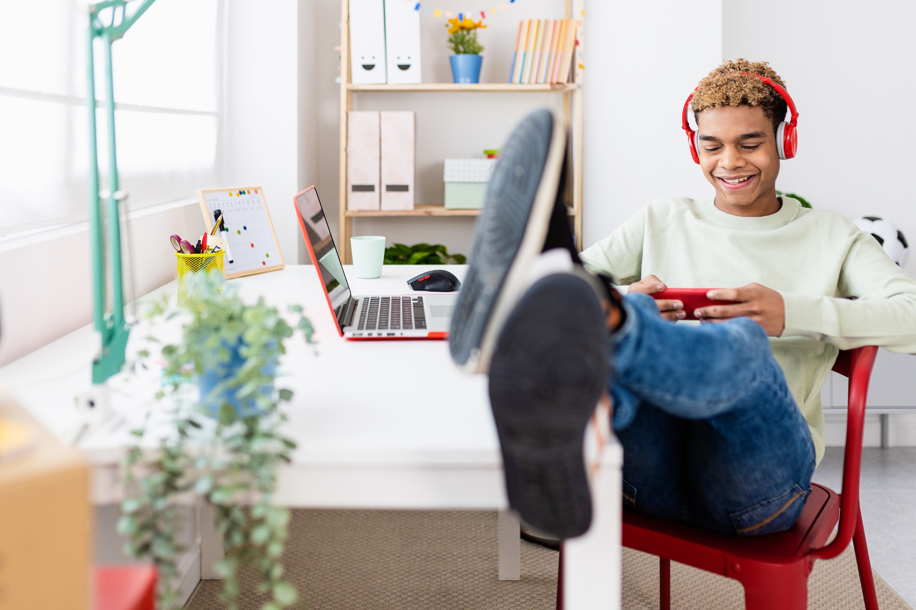 Young man sits in chair with headphones on watching his phone