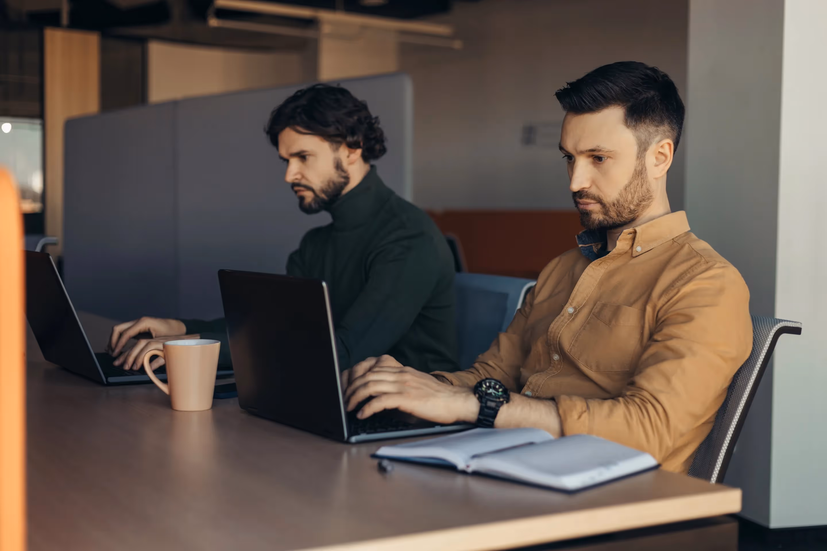 Two men at a table working on laptops, collaborating on IT service management for a non-profit organization.