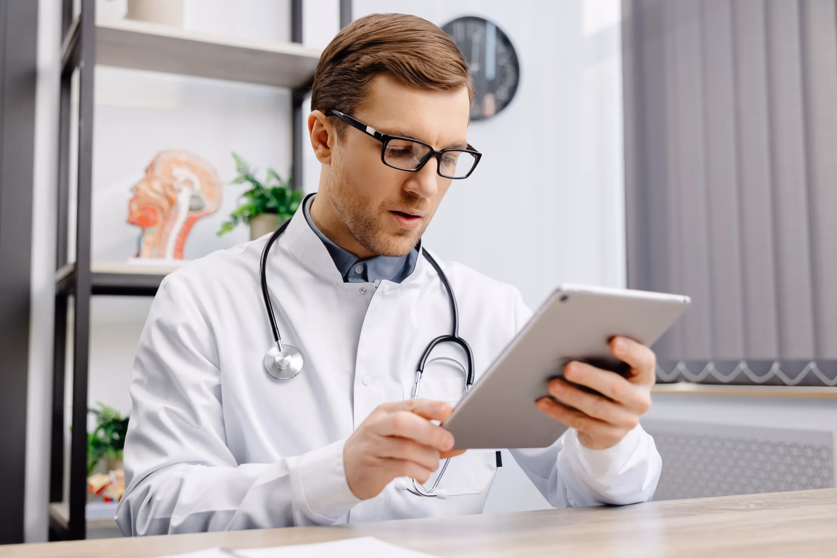 A male doctor in a white coat uses a tablet, symbolizing IT modernization in healthcare.