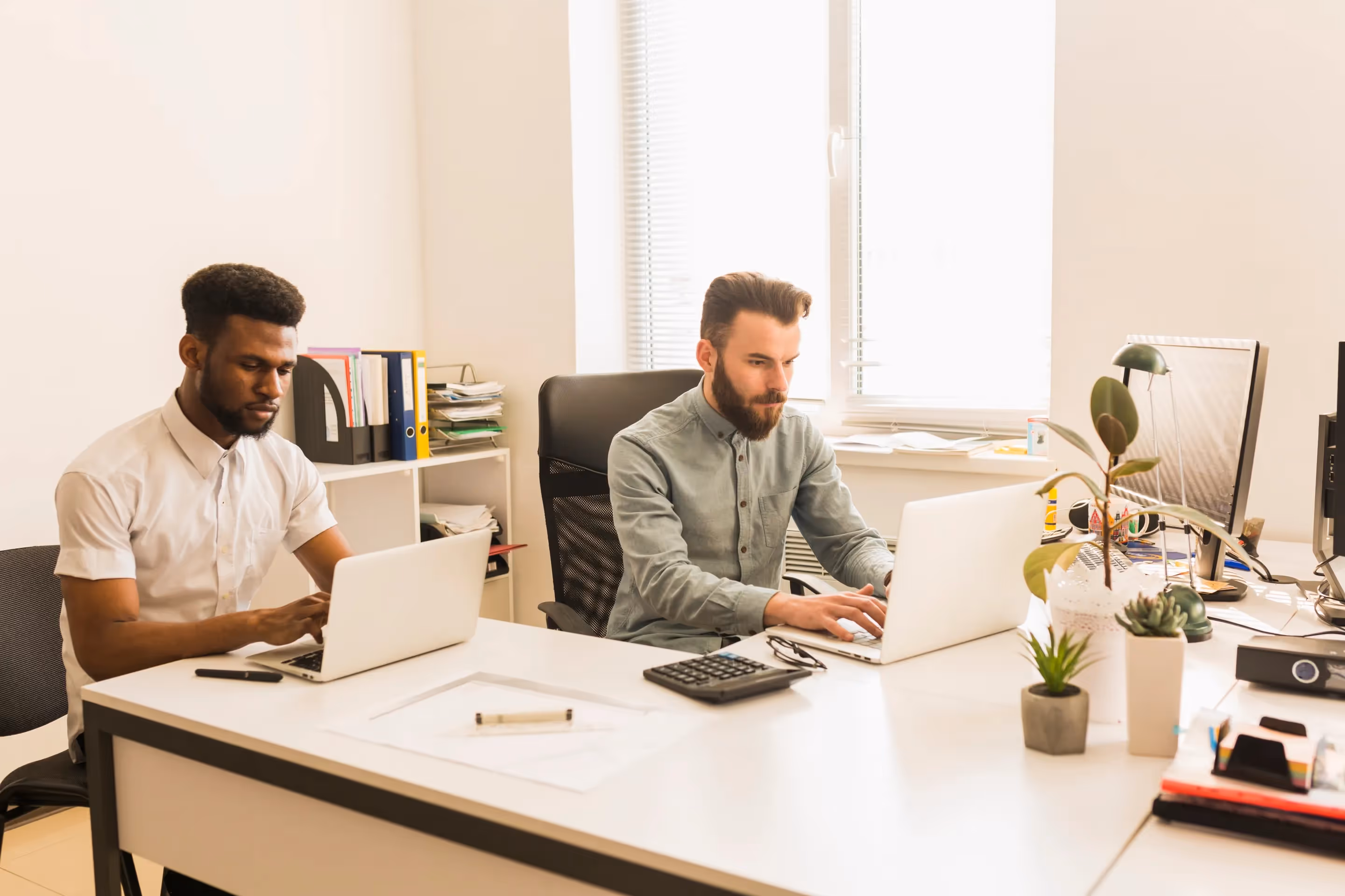 Two men working at a desk with laptops, discussing modern management solutions for relocation services in real estate.