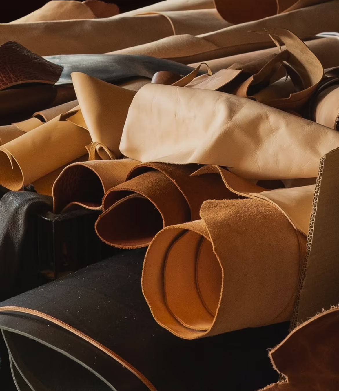 Rolled pieces of leather in various shades of tan, brown, and black piled together on a surface.