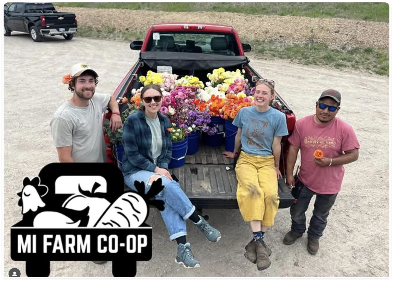 MI Farm Co-op workers pose with a farm truck loaded with fresh flowers and groceries.