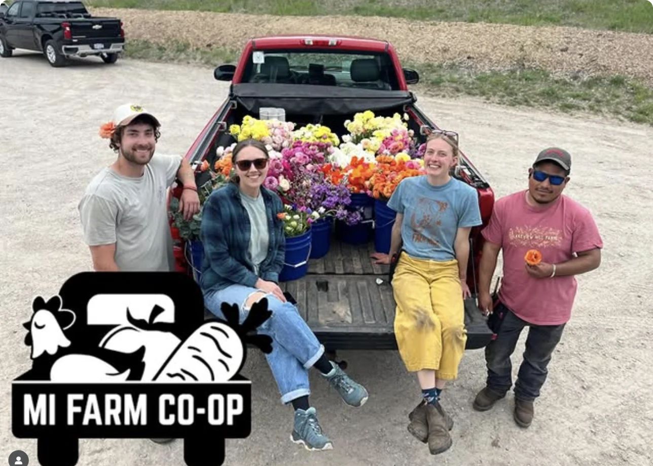 MI Farm Co-op workers pose with a farm truck loaded with fresh flowers and groceries.