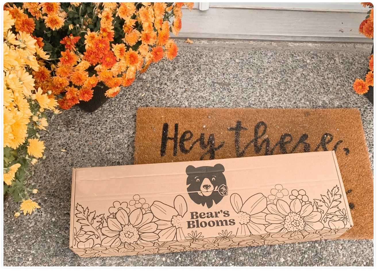 A flower delivery box with the Bear's Blooms logo rests on a customer's doorstep.