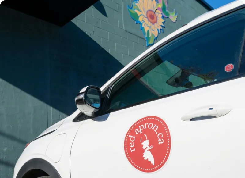 A Red Apron delivery car with the redapron.ca logo on the door