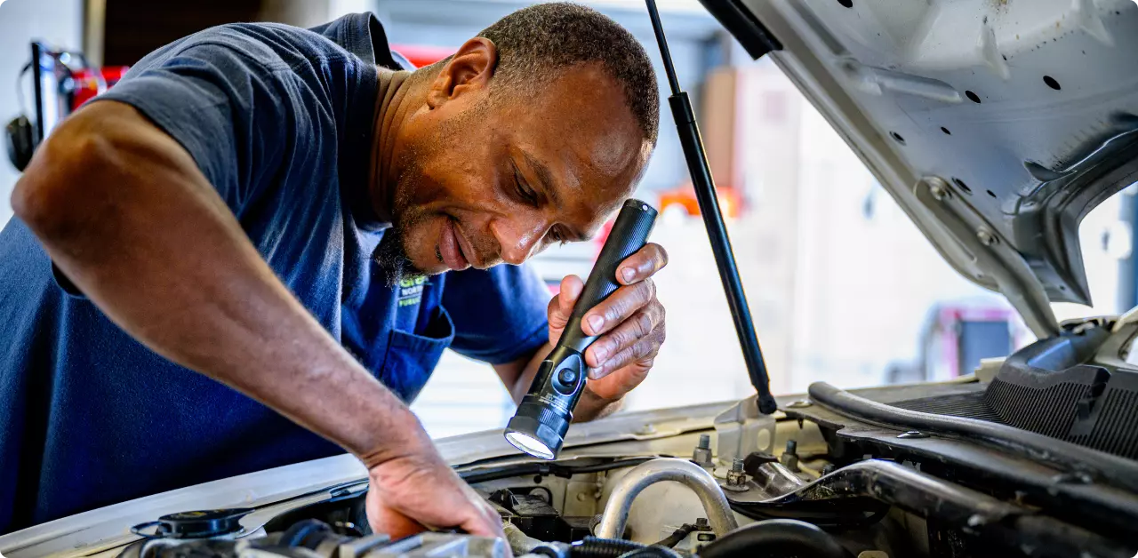 A mechanic uses a flashlight to inspect the engine of a delivery vehicle.