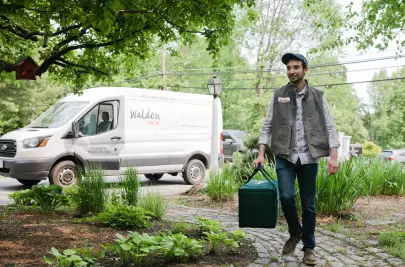 A delivery driver carries an insulated Walden Local bag from their company-branded delivery van to a customer’s door.