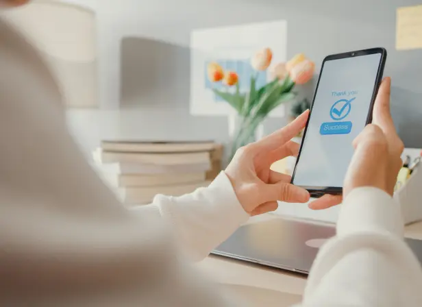 A woman’s hands holding a mobile phone. The screen displays a large check mark and the words “Thank you. Success.”