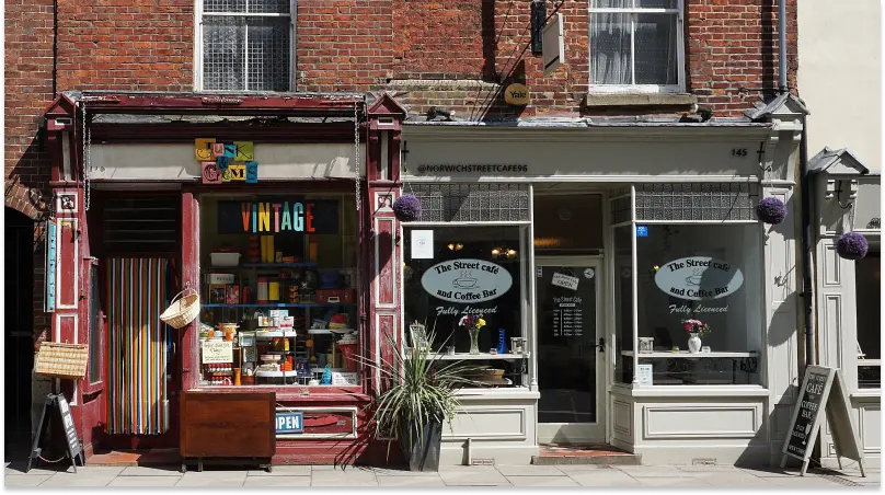 Streetscape showing small shops on the ground floor of an brick building. One has a colourful sign in the window saying “Vintage”. The other has signage saying “The Street Cafe and Coffee Bar”.