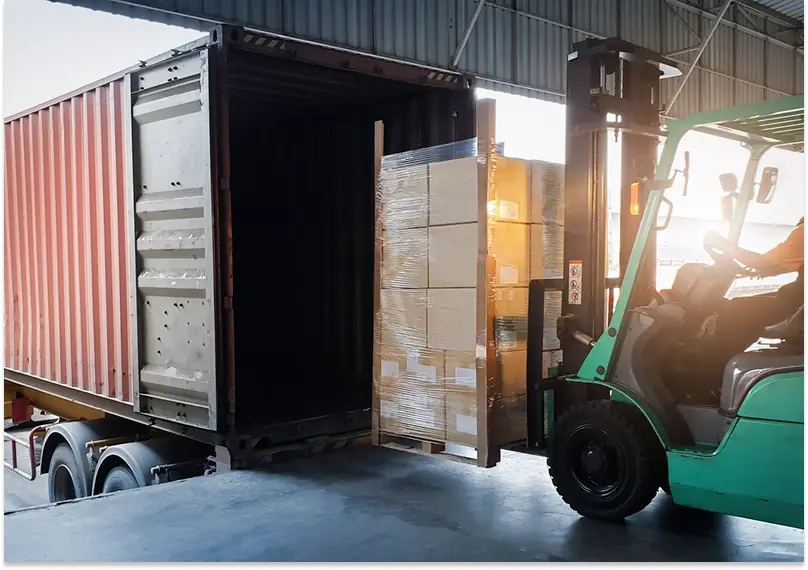A forklift driver loads a pallet onto a truck at a cross dock facility.
