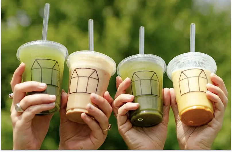 Close-up of four hands holding up different-coloured smoothies in branded Greenhouse Juice cups.