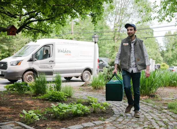 A delivery driver carries an insulated Walden Local bag from their company-branded delivery van to a customer’s door.