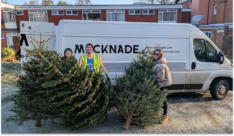 Volunteers pose with recycled Christmas trees in front of a truck from one of their corporate sponsors, Mackade.
