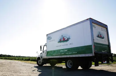 A branded 100km Foods truck on a farm road with fields in the background.
