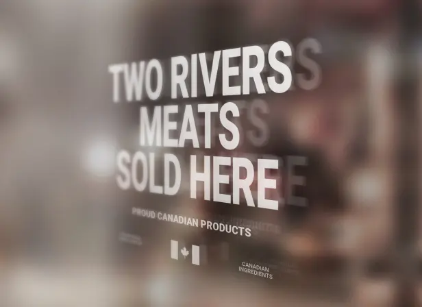 A sign painted on a window, reading "Two Rivers meats sold here. Proud Canadian products." There is a Canadian flag below, and in smaller text the words "Canadian ingredients".