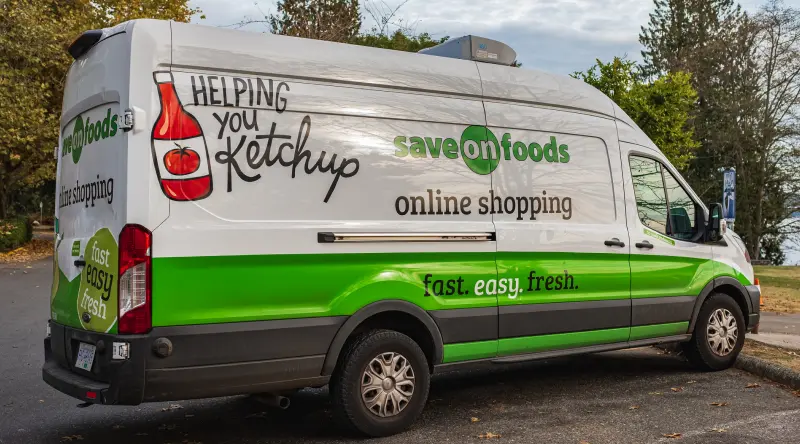 A grocery delivery van, with Save On Foods branding, parked with trees in the background.