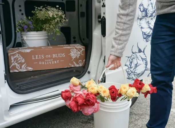 A Leis de Buds branded flower delivery box inside their delivery van, alongside buckets of fresh flowers.