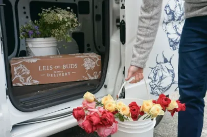 A Leis de Buds branded flower delivery box inside their delivery van, alongside buckets of fresh flowers.