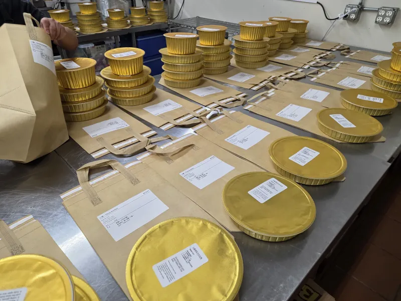Prepared dishes are sealed in gold foil containers, labelled and ready for packing into totes for delivery to customers.