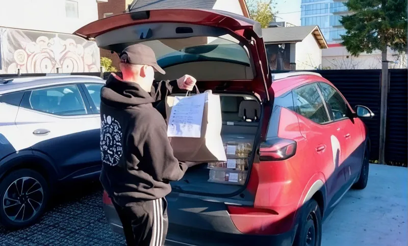 A Red Apron driver inspects the delivery label on a bag as he loads it into his car for delivery