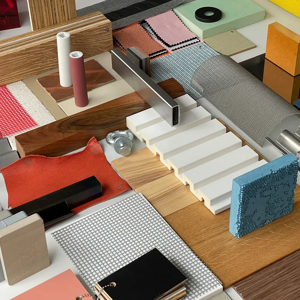 Material collage featuring various construction and design samples, including wood and metal pieces, meshes, textiles, and colored panels. The arrangement showcases a variety of surface textures and materials in different colors and shapes.