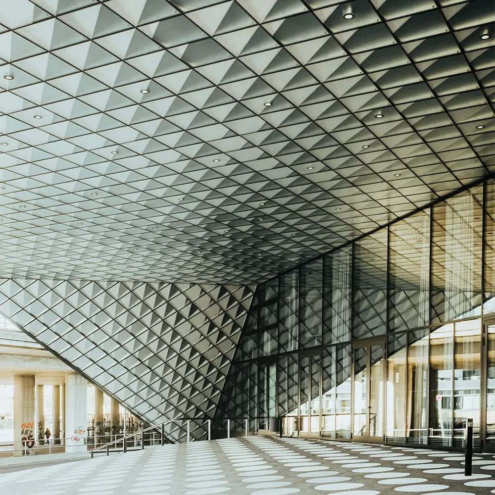 Ein modernes Gebäude, das mit Glas und weißen Fliesen gefüllt ist. Das Design folgt dem Stil ephemeraler Muster mit scharfen und kantigen Linien. Die Deckengestaltung ist kunstvoll und komplex. Die Atmosphäre ist leicht verschwommen und erzeugt eine gewisse Hazy-Stimmung.