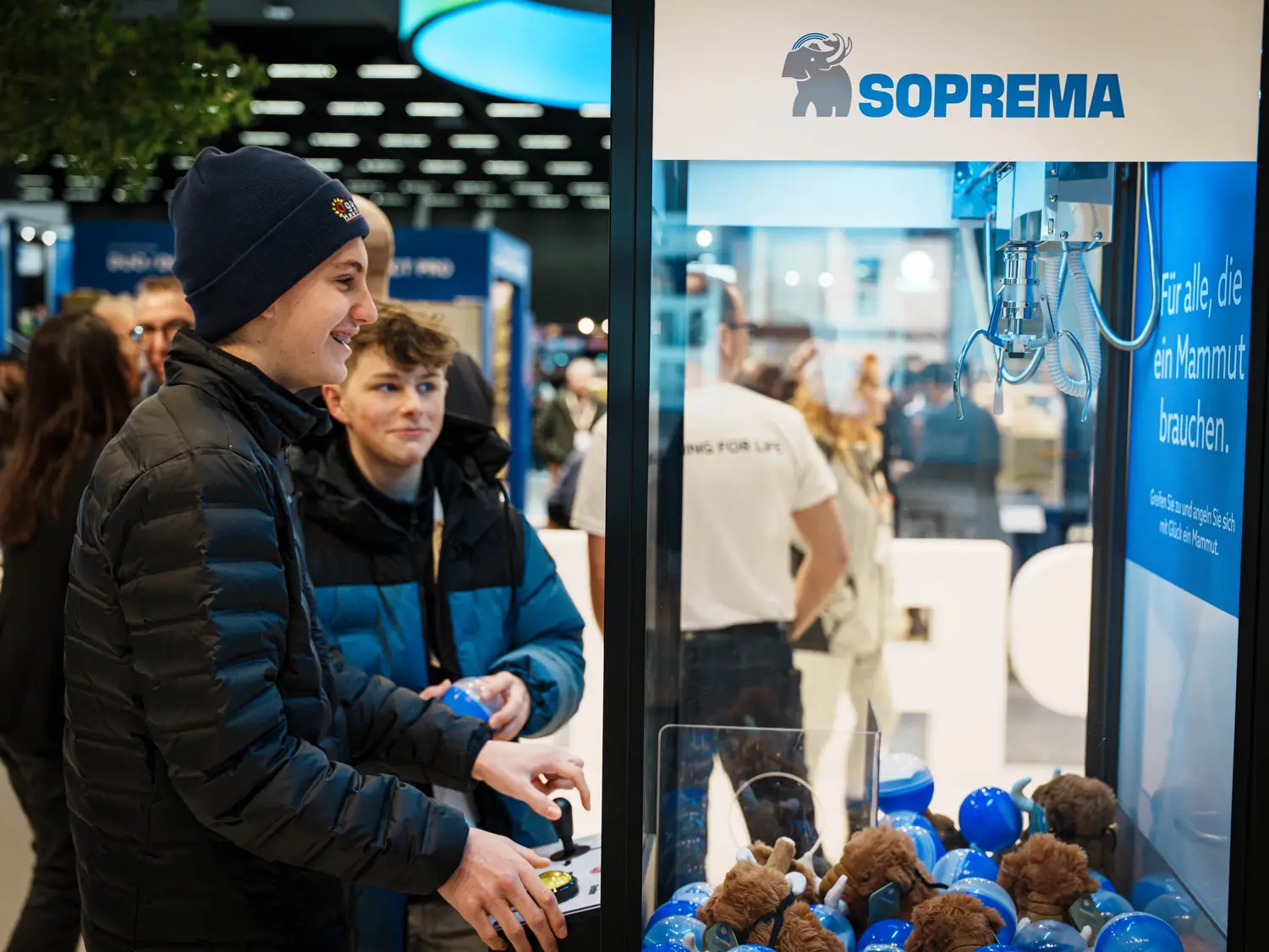 Besucher:innen interagieren mit einem Greifautomaten am Soprema-Messestand auf der Swissbau 2026.