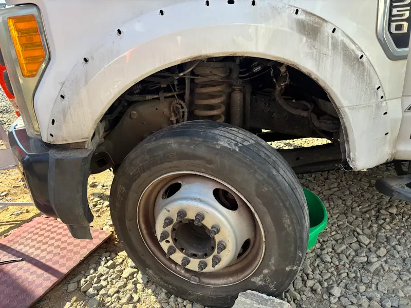 Wheel hub repair on heavy-duty truck with exposed lug studs and suspension components during service on gravel surface.