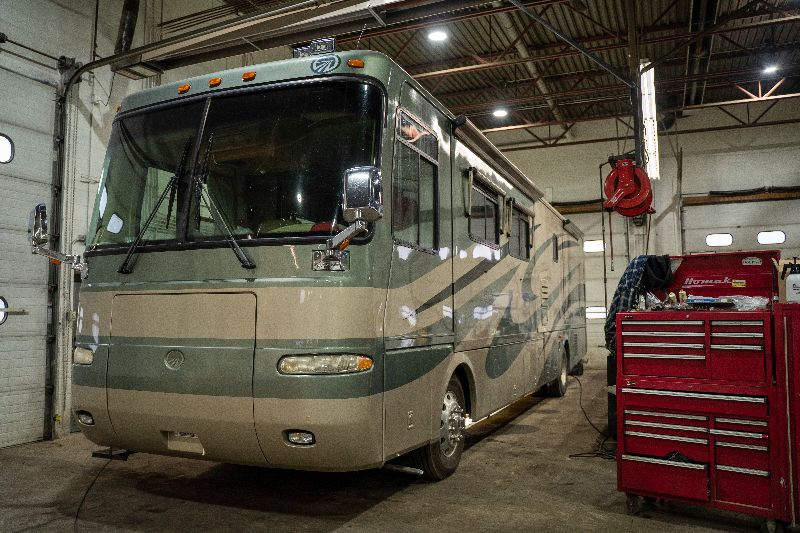 Large beige motorhome parked inside a repair shop with tools, red toolbox, overhead lights, and industrial garage setting clean spacious