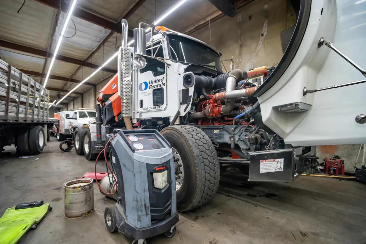 HVAC service on a heavy-duty truck with open hood and diagnostic equipment during maintenance in a repair shop.