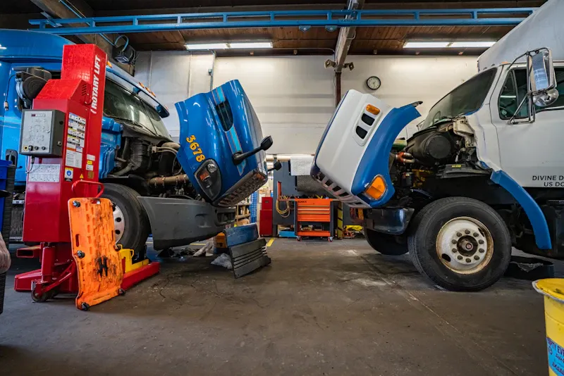 Truck breakdown repair service in a heavy-duty shop with two commercial trucks undergoing diagnostics and mechanical repairs with hoods raised.